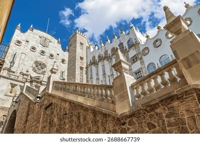 Historic white stone buildings with ornate Gothic architecture and defensive towers against blue sky